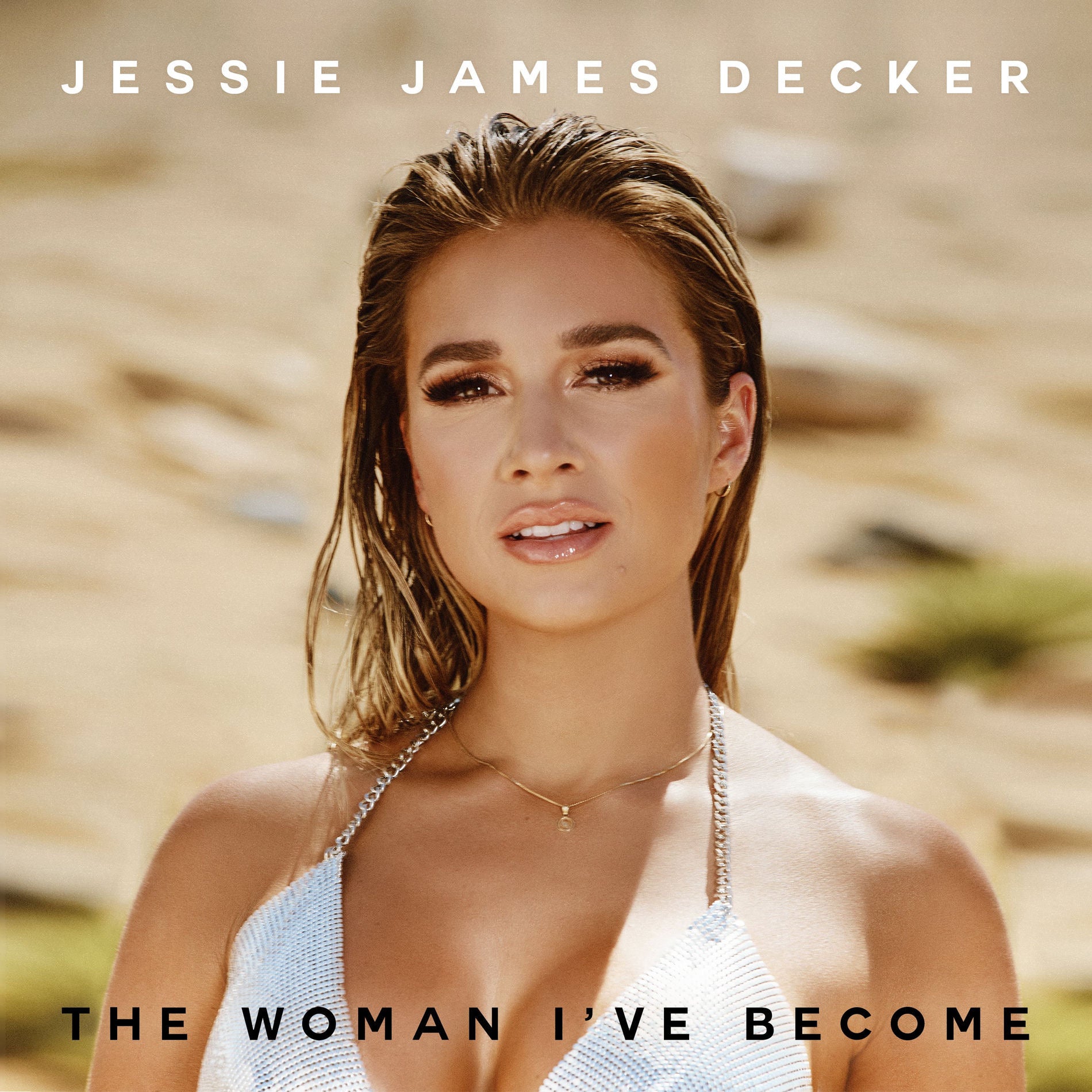 Album cover for Jessie James Decker's 'The Woman I've Become', featuring a portrait of the artist against a blurred sandy background with text at the top and bottom.
