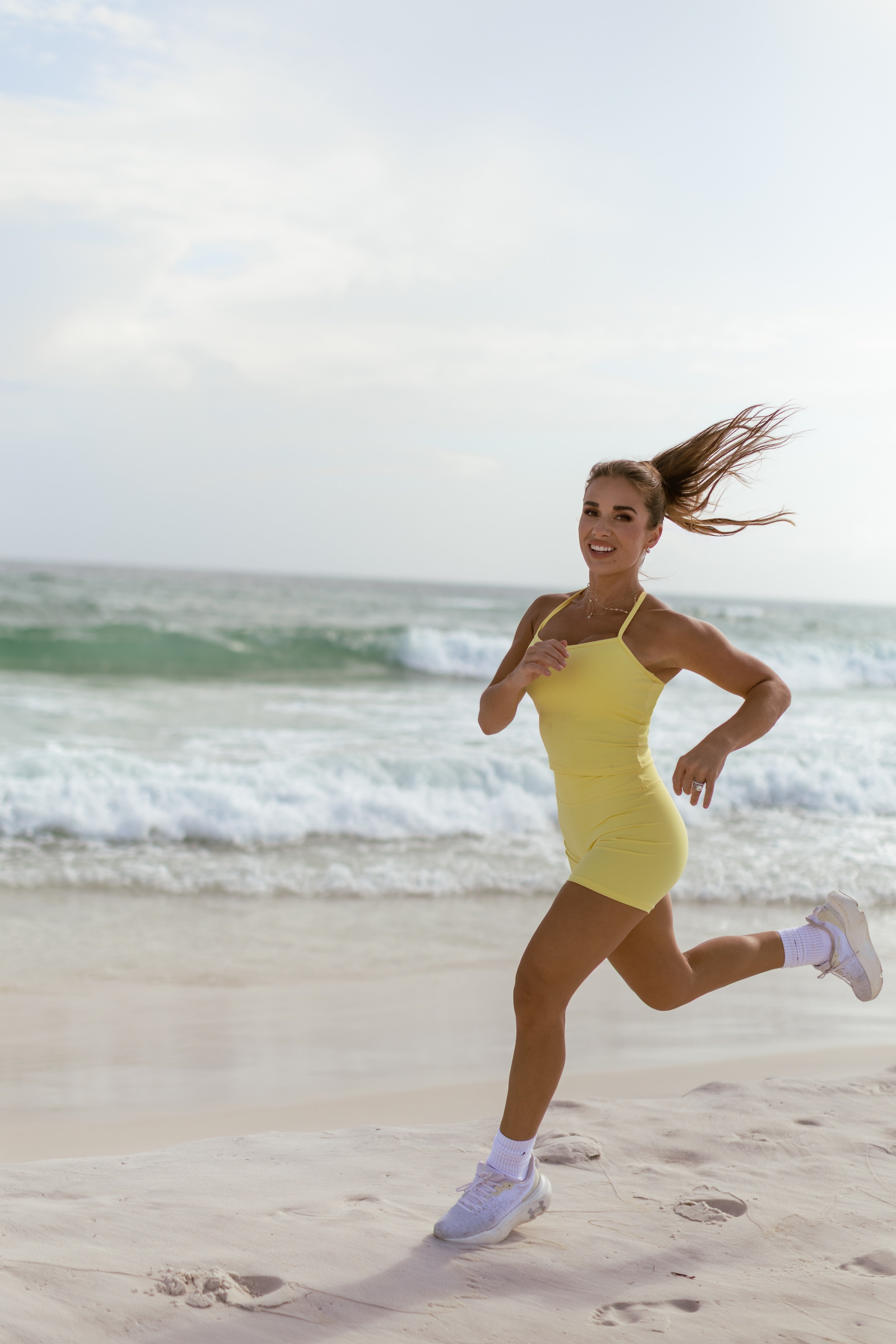 Jessie running on a beach wearing a yellow workout set.