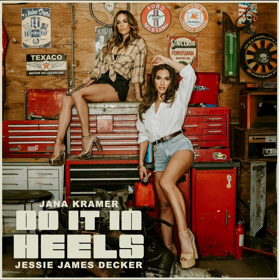 A promotional graphic for Jana Kramer's 'Do It In Heels' featuring Jessie James Decker. The image shows two women posing in a rustic garage workshop setting with red toolboxes and vintage signs.
